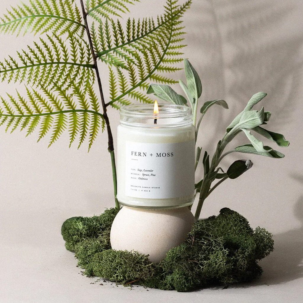 Fern + Moss candle with greenery on a neutral background