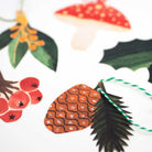 Close up of set of Christmas-themed gift tags including a mushroom, holly, pine cone, and berries on a white background.