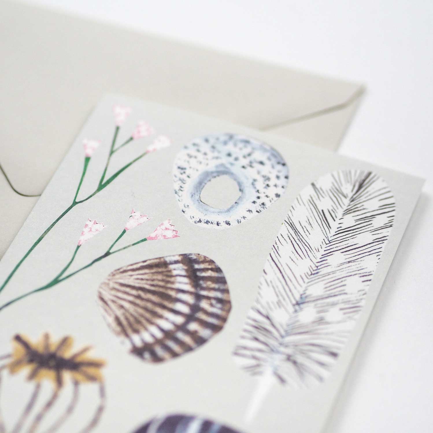 Greeting card with nature-themed design featuring a shell, flowers, and leaves on a white background.