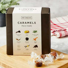Box of McCrea's Caramels on a wooden board with caramels around it.