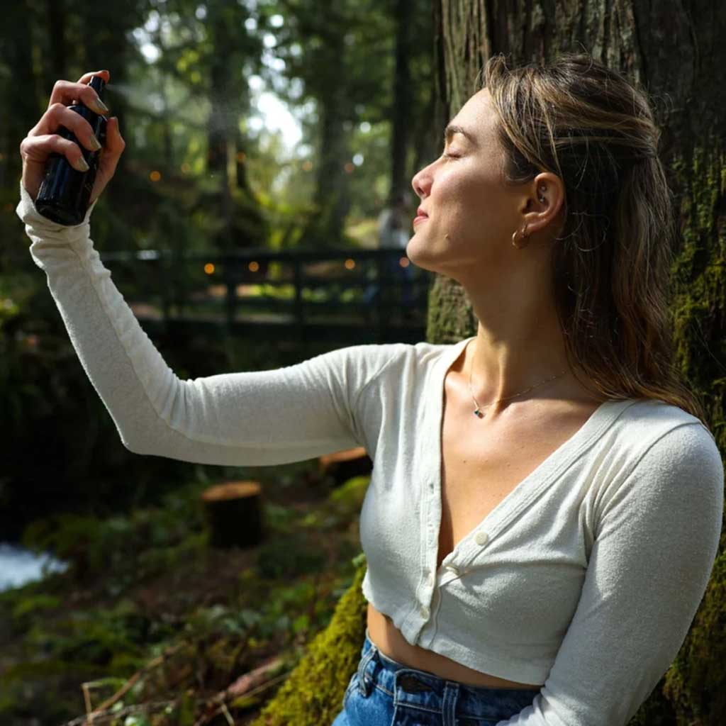 Woman applying spray facial toner in a forest setting