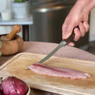 Person cutting fish fillet on a wooden board with a knife in a kitchen setting.