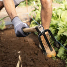 Person gardening with a forked hoe tool in a garden setting
