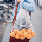 Person holding a string bag filled with oranges on a blurred street background