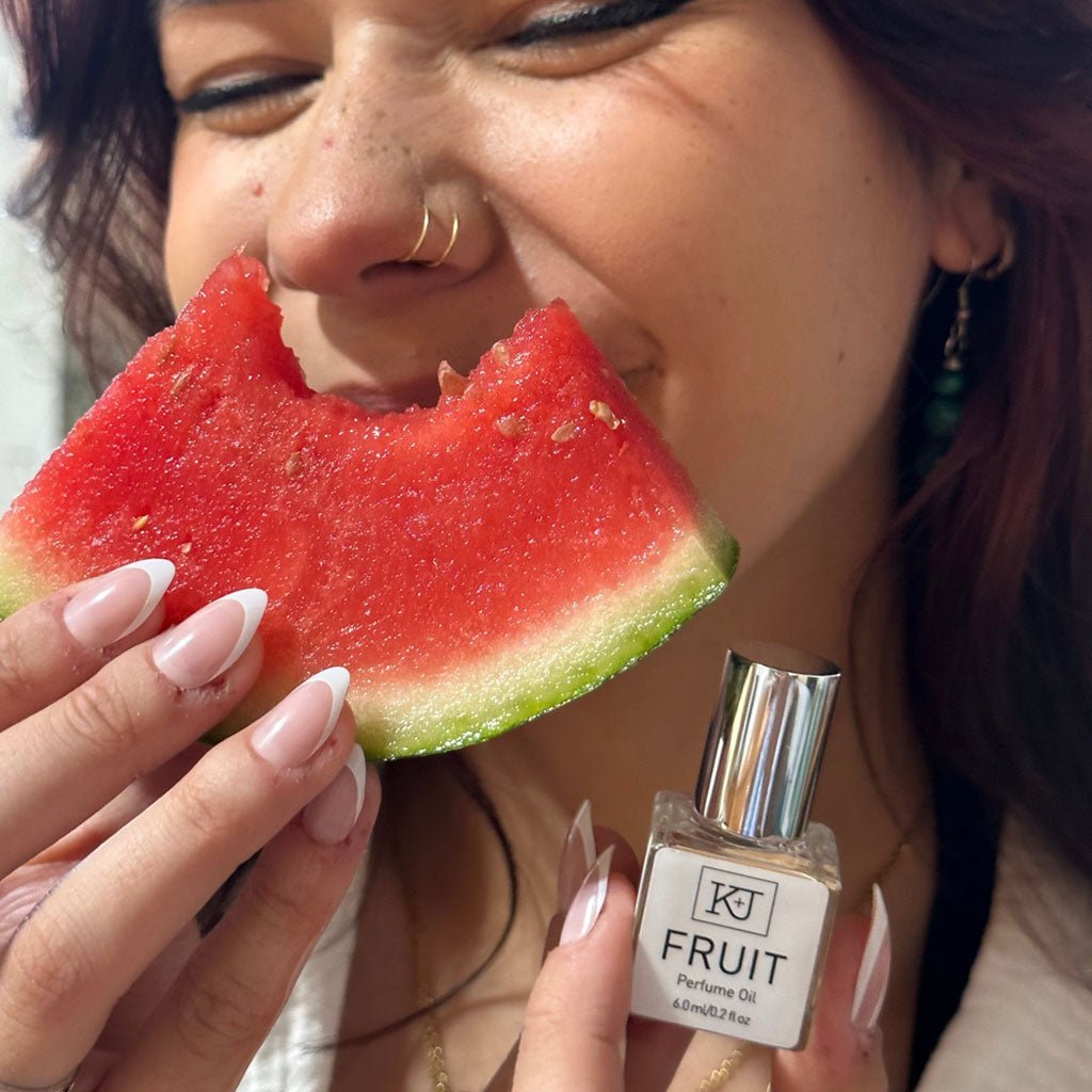 Woman holding a slice of watermelon and a perfume bottle labeled fruit