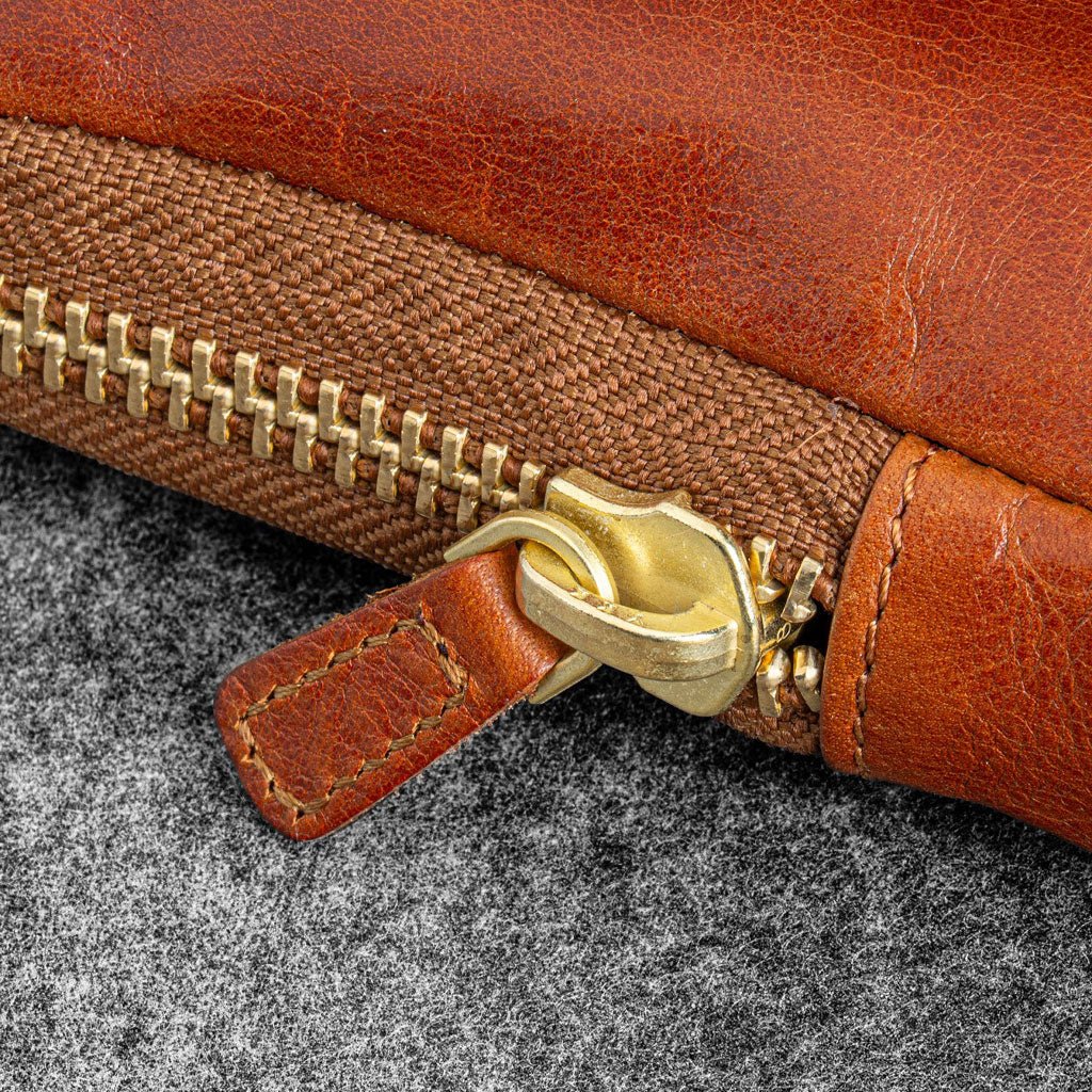 Close-up of a brown leather bag with a gold zipper on a gray surface