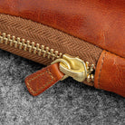 Close-up of a brown leather bag with a gold zipper on a gray surface