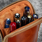 Brown leather pouch with gold zipper containing various pens.