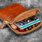 Brown leather pouch with gold zipper, containing notebooks and pens, on a gray textured background.