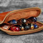 Open brown pouch with gold zipper containing various pens and a 'Nock' label on a gray background