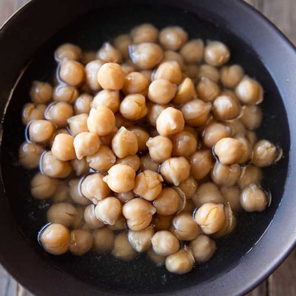 Chickpeas soaking in a dark bowl on a wooden surface