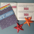 Open book with origami instructions and two folded paper stars on a blue surface