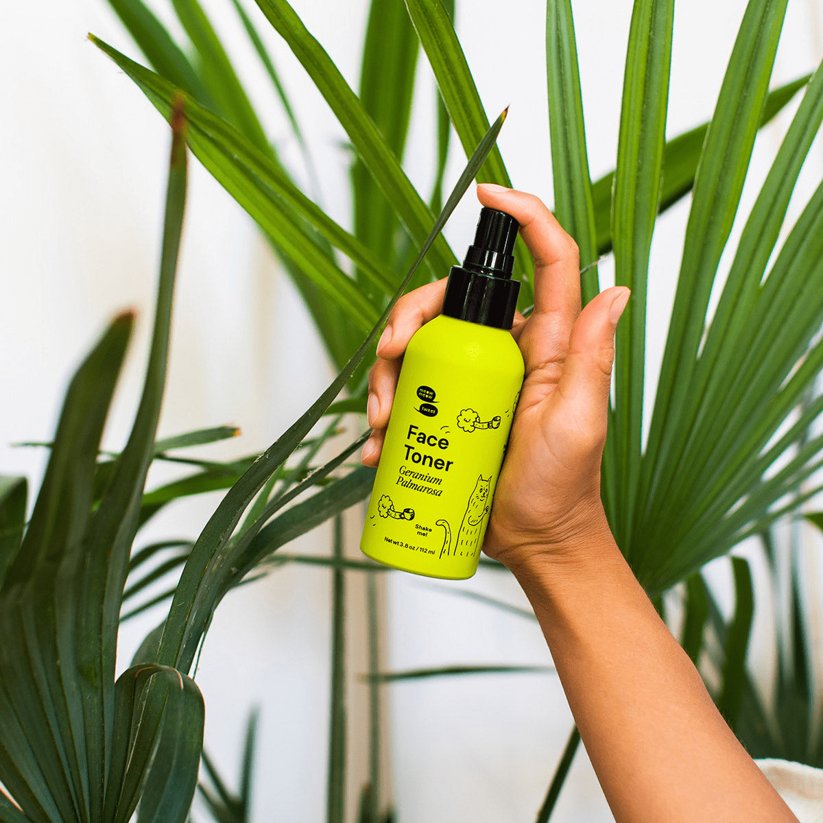 Hand holding green spray bottle of face toner in front of green plants