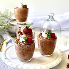 Three small glass cups filled with chocolate mousse and topped with raspberries and mint leaves on a white plate.