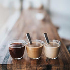 Three glasses of different types of coffee on a wooden table.