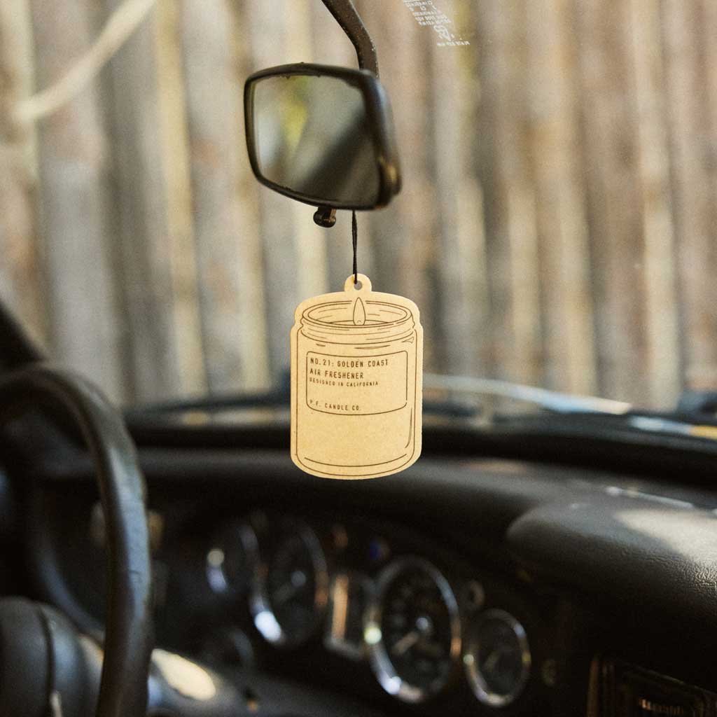 Car air freshener hanging from a mirror with a blurred forest background