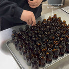 Person arranging brown bottles on a tray with text 'Made in Los Angeles by our team.'