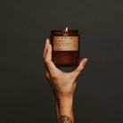 Hand holding a lit amber candle against a dark background
