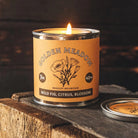Candle in a 'Golden Meadow' tin on a wooden surface with a dark background
