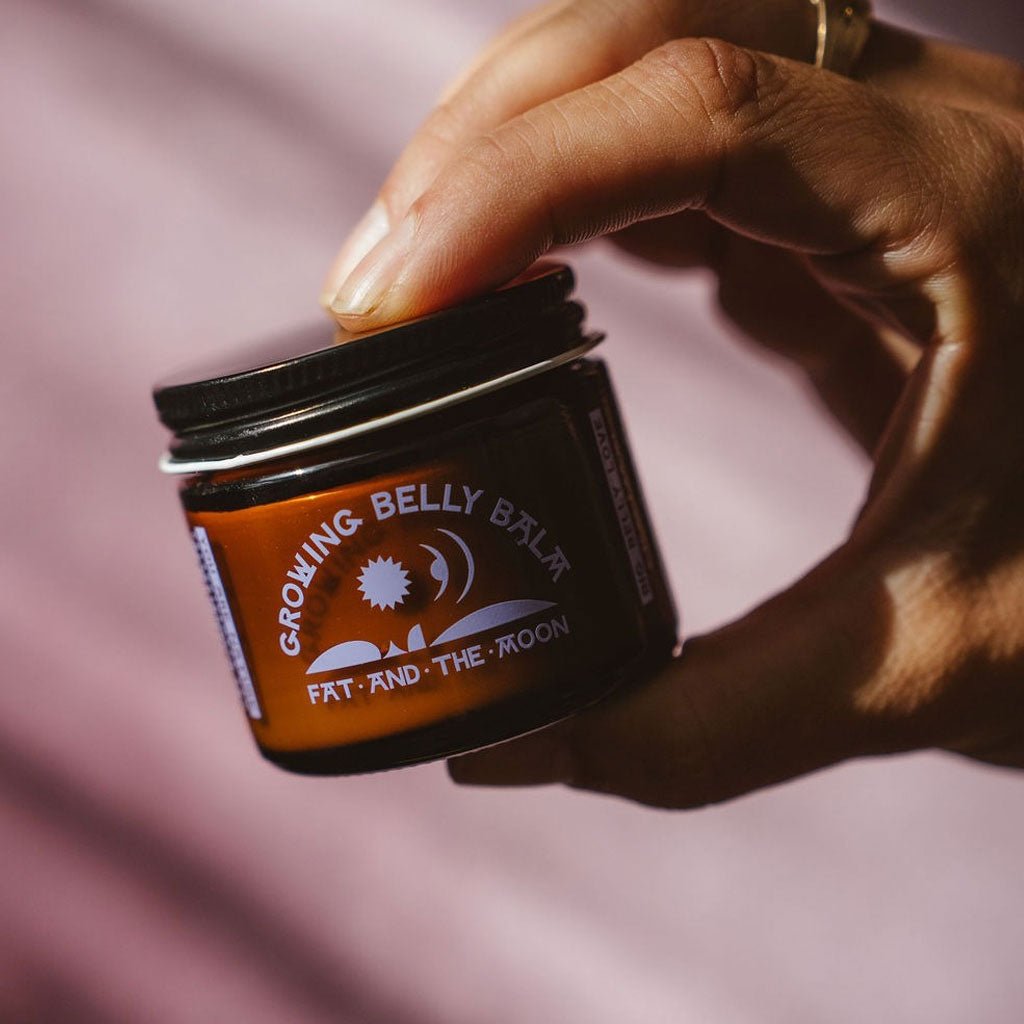 Hand holding a jar of Growing Belly Balm