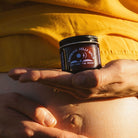 Person holding a jar of 'Growing Belly Balm' against a yellow shirt.