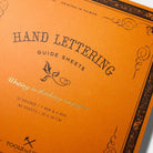 An orange Hand Lettering Guide Sheets pad on white background