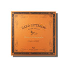 An orange Hand Lettering Guide Sheets pad on white background