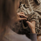 Close-up of hands holding a knitted item with a textured blanket in the background.