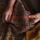 Close-up of hands holding patterned knit fabric with warm colors.
