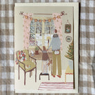 A holiday card with illustration laying on gingham fabric.