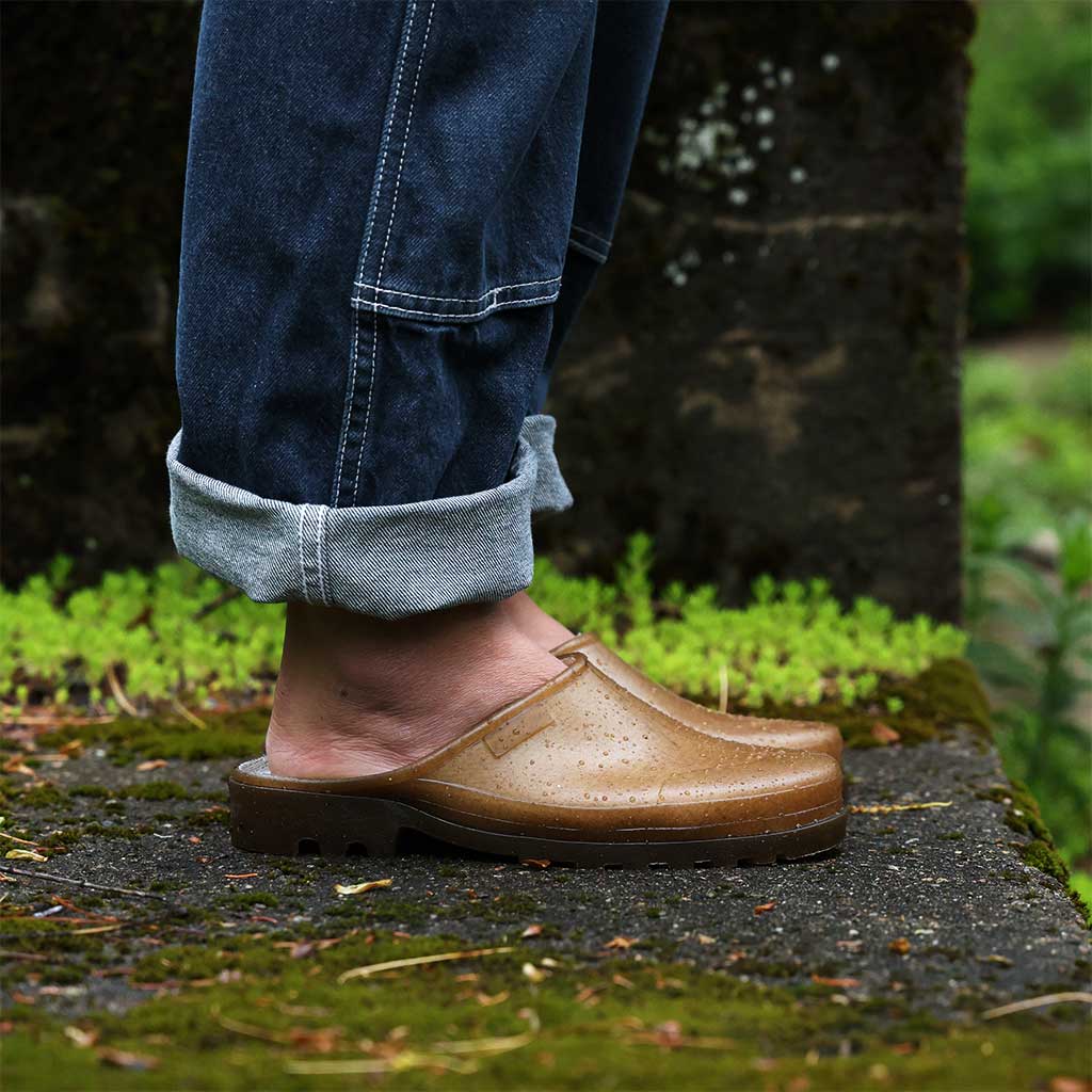Person wearing brown hemp mules with rolled-up jeans on a natural background