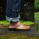 Person wearing brown hemp mules with rolled-up jeans on a natural background