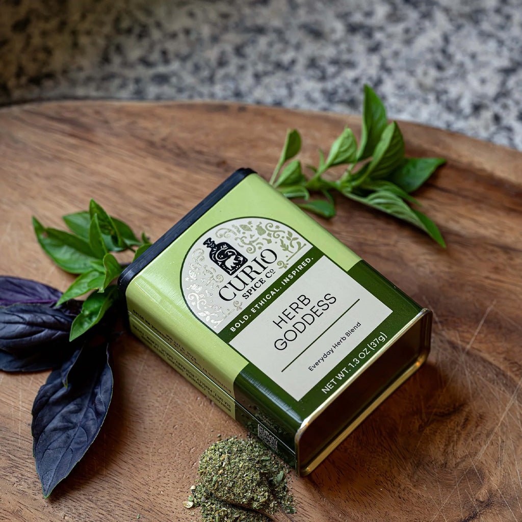 Green tin of herb goddess seasoning blend on wooden cutting board next to ingredients