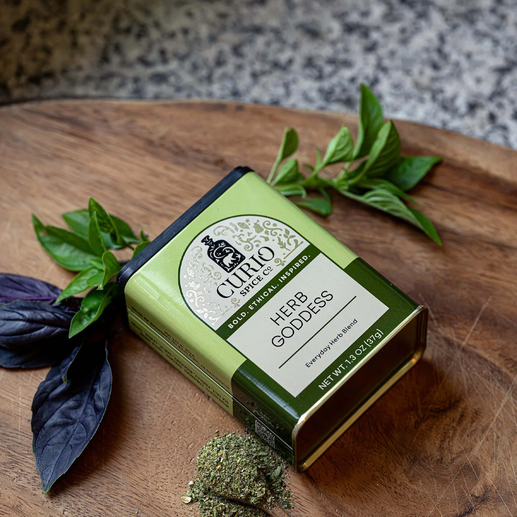 Green tin of herb goddess seasoning blend on wooden cutting board next to ingredients