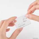 A close-up of hands holding a transparent acrylic block with a clear embossed stamp with a Moomin character design, shown against a plain white background.