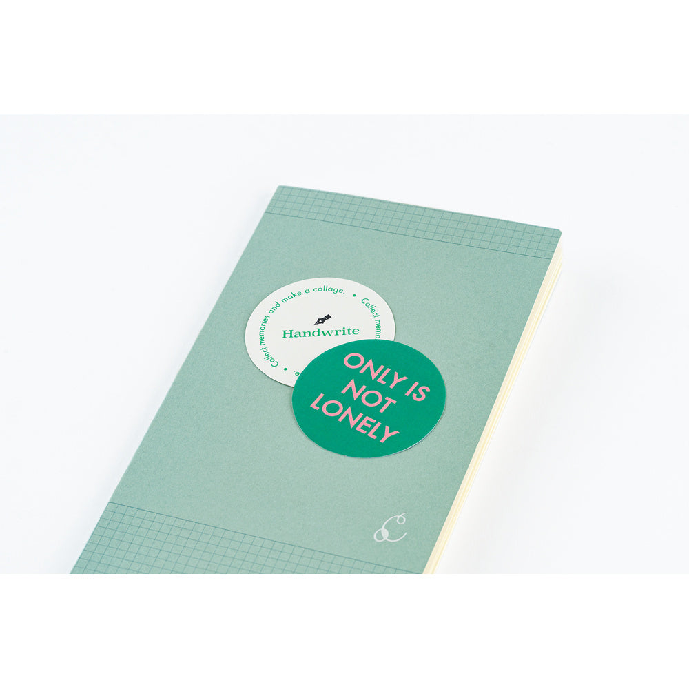 A mint green notebook with a grid pattern, featuring a green circular sticker that reads 'ONLY IS NOT LONELY' and a white circular sticker that reads 'Handwrite'.