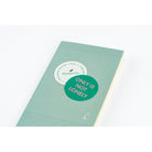 A mint green notebook with a grid pattern, featuring a green circular sticker that reads 'ONLY IS NOT LONELY' and a white circular sticker that reads 'Handwrite'.