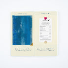 An open paper journal with cream-colored grid pages, featuring a blue abstract art print on the left page and a printed receipt styled as a postmark on the right page.