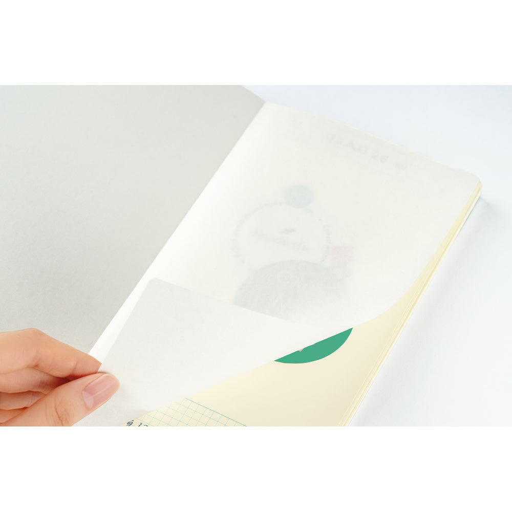 A hand opening a cream-colored notebook or journal, showing a pale yellow interior page and faint printed illustration.