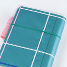 Clear cover on teal blue A6 Hobonichi Techo cover with colorful dotted plaid pattern against white background