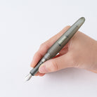 A hand holding a translucent gray fountain pen with a silver nib against a clean white background.