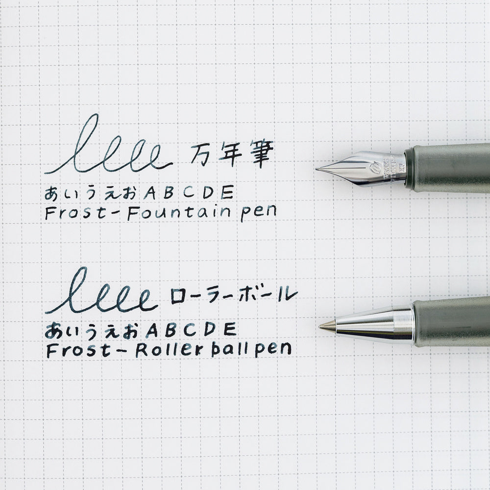Two pens, one with a fountain pen nib and one with a Rollerball nib, shown on a white graph paper background with sample handwritten Japanese text and English transliterations.