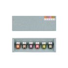 A set of six small glass ink bottles with silver caps arranged in a light gray presentation box, shown below the matching box lid. The bottles have color labels numbered 1 through 6.