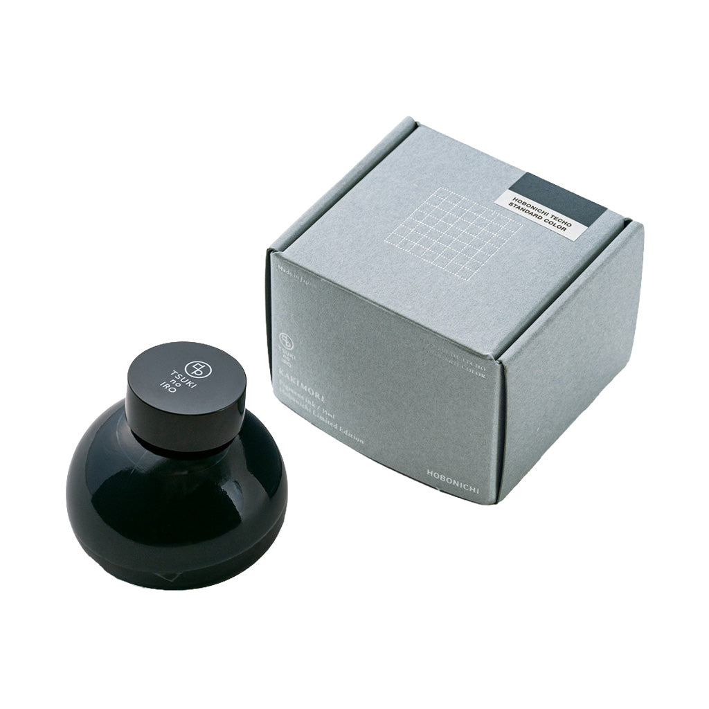 Dark blue bottle of ink with cap that has TSUKI no IRO branding, next to gray rectangular box on white background