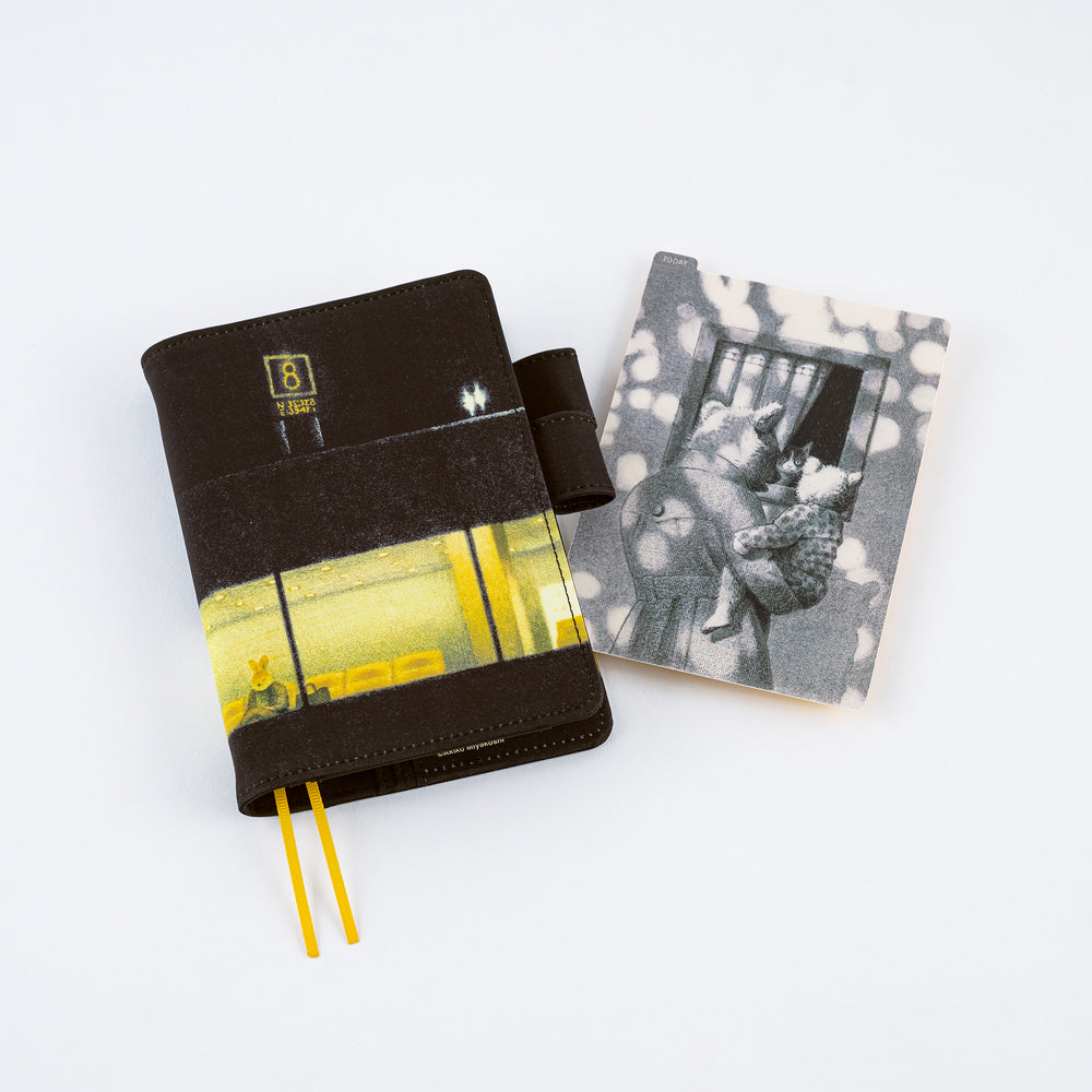 A dark planner with a yellow and black airport terminal cover design, shown next to its matching black-and-white pencil board on a clean white background.