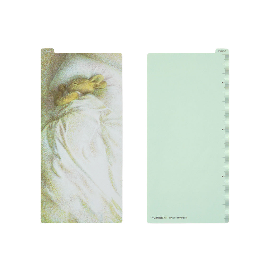Front and back of rectangular pencil board for Hobonichi Techo weeks on white background. The front design has a drawing of a rabbit sleeping in bed with white bedsheets, and the back is a plain mint green color.