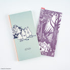 A mint green 2026 Moomin Techo Weeks notebook with black line art illustrations of characters, shown next to a matching purple pencil board featuring a forest scene, on a clean white background.