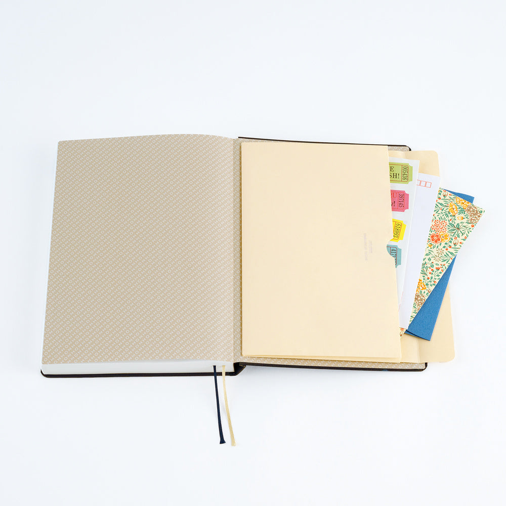 An open A5 Hobonichi Techo planner with cream paper pocket envelope open with stationery supplies on white background