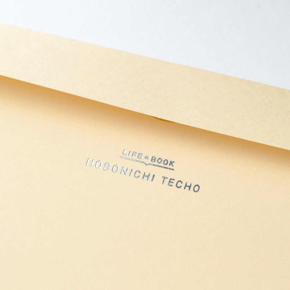 A close-up of a light beige paper envelope with the text 'LIFE BOOK' and 'HOBONICHI TECHO' printed in silver on the flap.