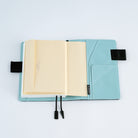 An open light blue planner or notebook cover with cream-colored pocket envelope inserted, shown on a clean white background. 